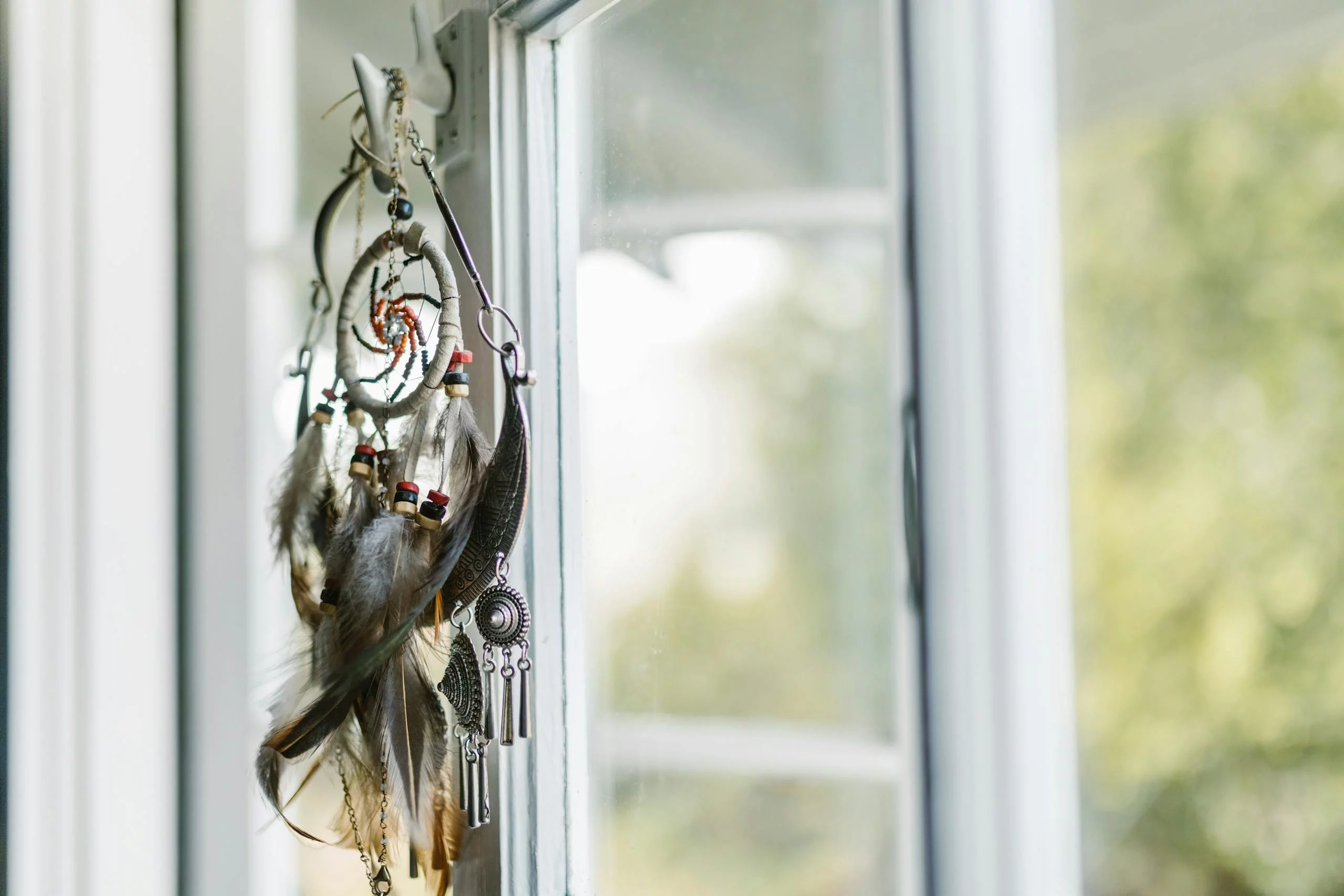 A dreamcatcher with feathers hangs by a sunlit window